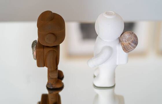 RAWbot und weisser UStronaut R&uuml;cken an R&uuml;cken auf einer Spiegelfl&auml;che.