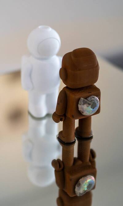 RAWbot und UStronaut spiegeln sich auf einer gl&auml;nzenden Fl&auml;che.