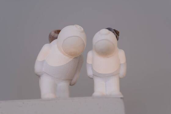 Zwei UStronauts auf einem Sockel, die K&ouml;pfe einander zugeneigt, warmes Licht.