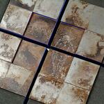 Eight rusty plates arranged in a cross with fine drawings on a dark ground with blue joints.