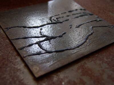 Close-up of a dark metal plate with a fine line drawing scratched into it.