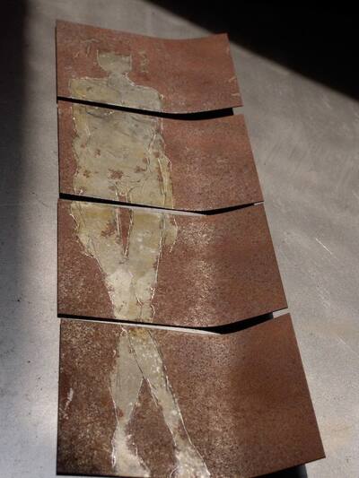Four curved rust plates from which a light figure emerges.