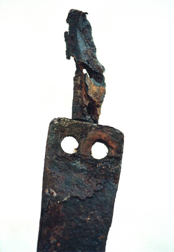 Rusty forged metal object with two holes against a white ground.