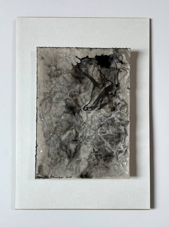 Grey, crumpled surface with black ink marks, mounted on white card.