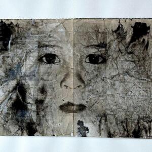 Mit schwarzer Tusche gezeichnetes Gesicht auf zerknittertem Papier, mittig gefaltet.