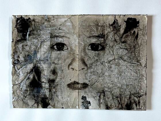 Face drawn in black ink on crumpled paper, folded down the middle.