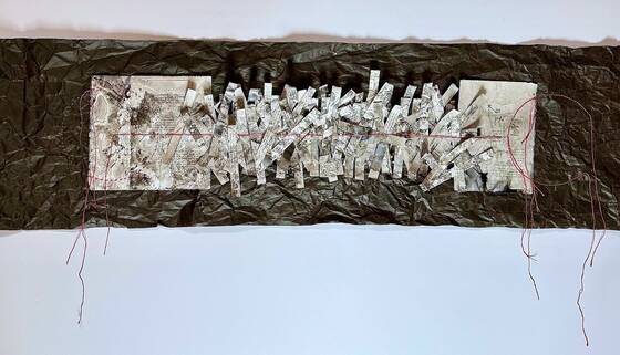 Long, narrow work: strips of paper with writing on black, crumpled paper, red threads hanging from the ends.