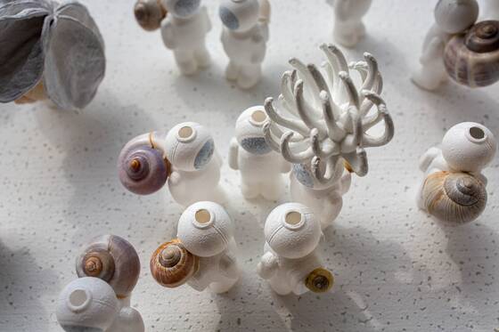 View from above of UStronauts and a white coral-like sculpture, with small snail shells in between.