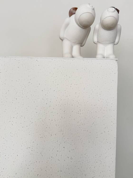Two small UStronauts on a white plinth leaning towards each other.
