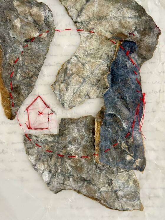 Detail of a paper work: pieces of stone on handwritten paper, a red house and a circle of red thread.