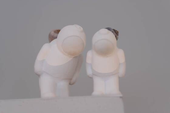 Two white UStronauts stand close together, their heads tilted towards each other.