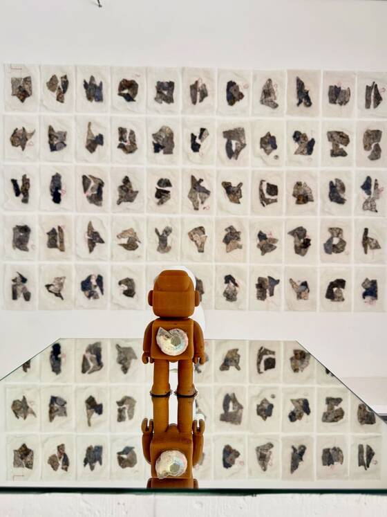 RAWbot on a mirrored surface in front of a wall of small paper works.