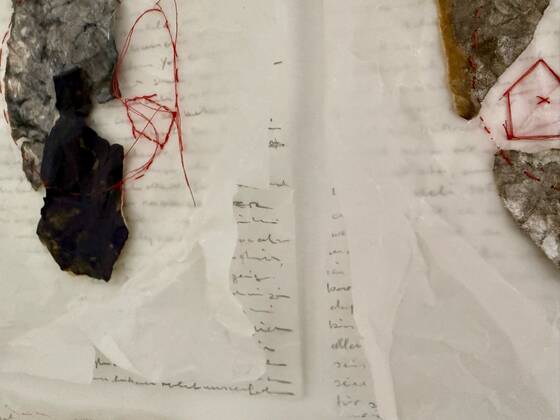 Detail of a paper work: dark pieces of stone on handwritten paper, a drawing in red thread.