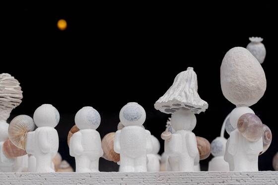 UStronauts in a row against a black background, some with mushroom, poppy-capsule or egg shapes on their heads.