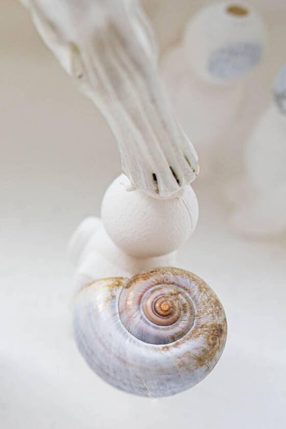 Close-up of a figure carrying a softly shimmering snail shell, a white structure reaching in from above.