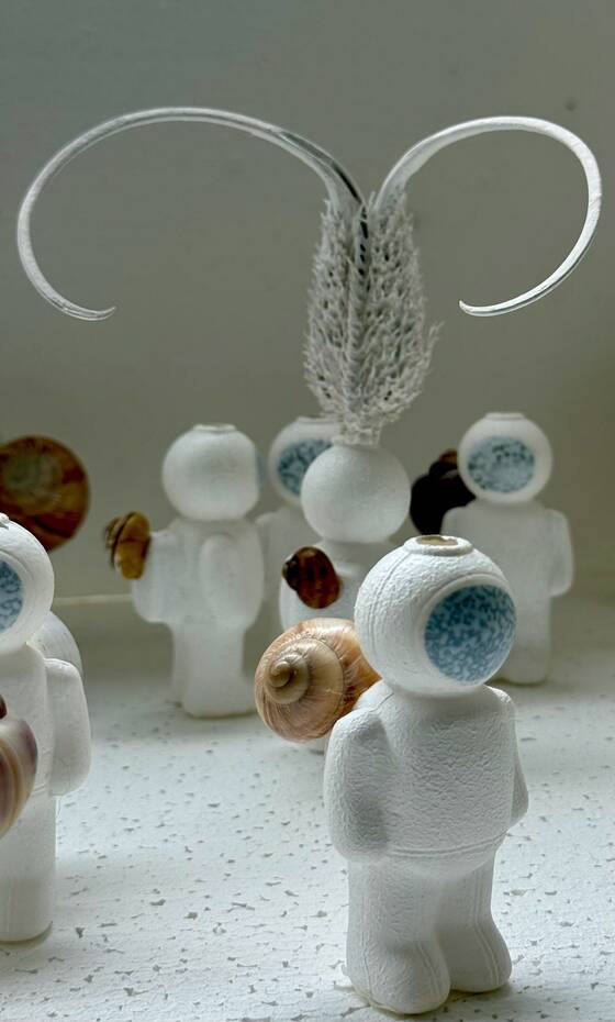 UStronaut in the foreground, figures with glass and feather-like forms behind it.