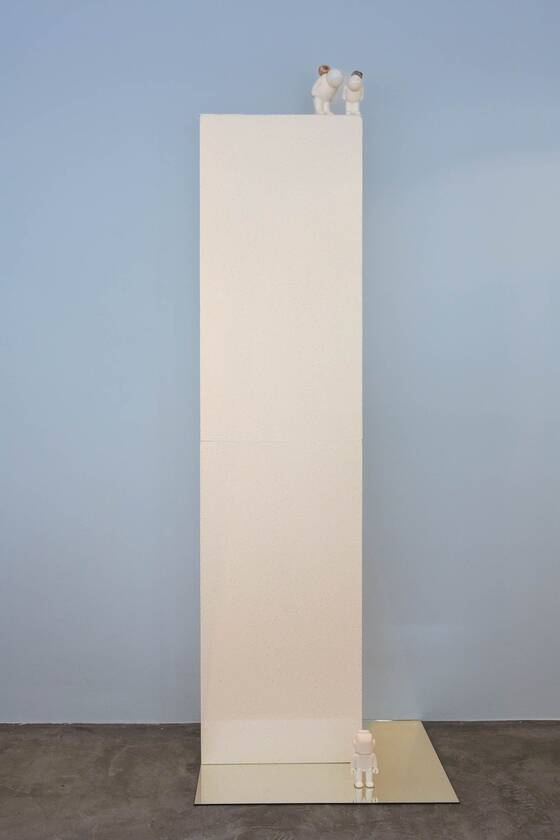 Tall white plinth against a blue wall, with two tiny UStronauts at the very top.
