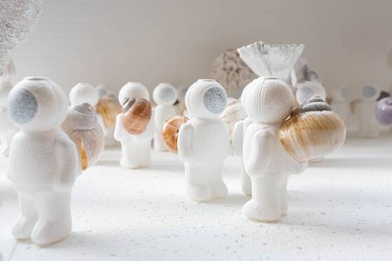 Side view of UStronauts with patterned snail shells, a glass form in the background.