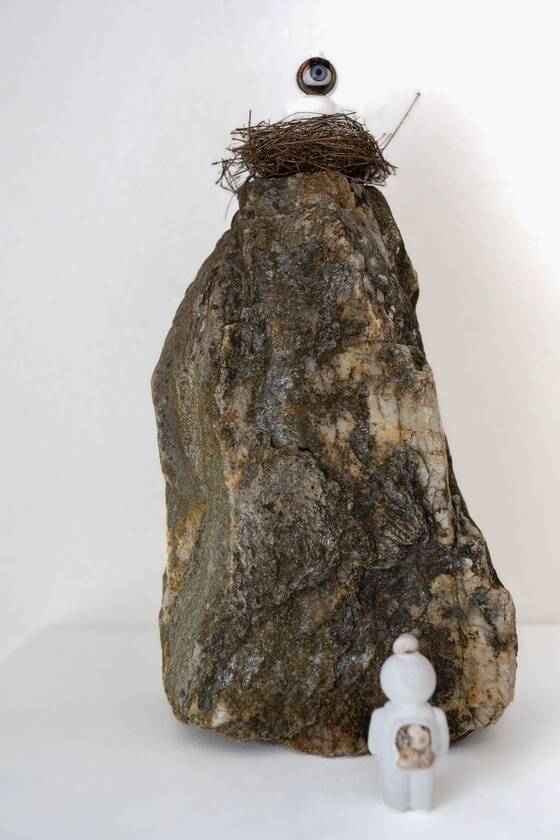 Large stone with a nest and a UStronaut on top, a small white figure standing at its foot.