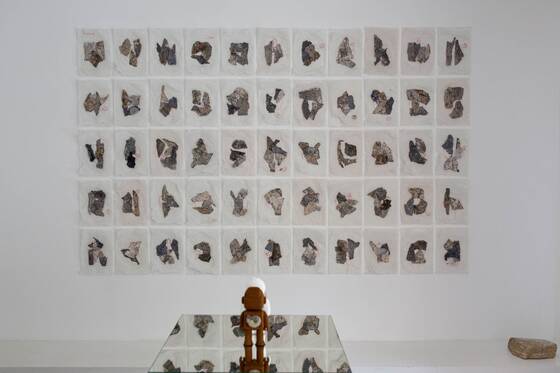 Wall of around sixty small paper works, a RAWbot on a mirrored surface in front of it.